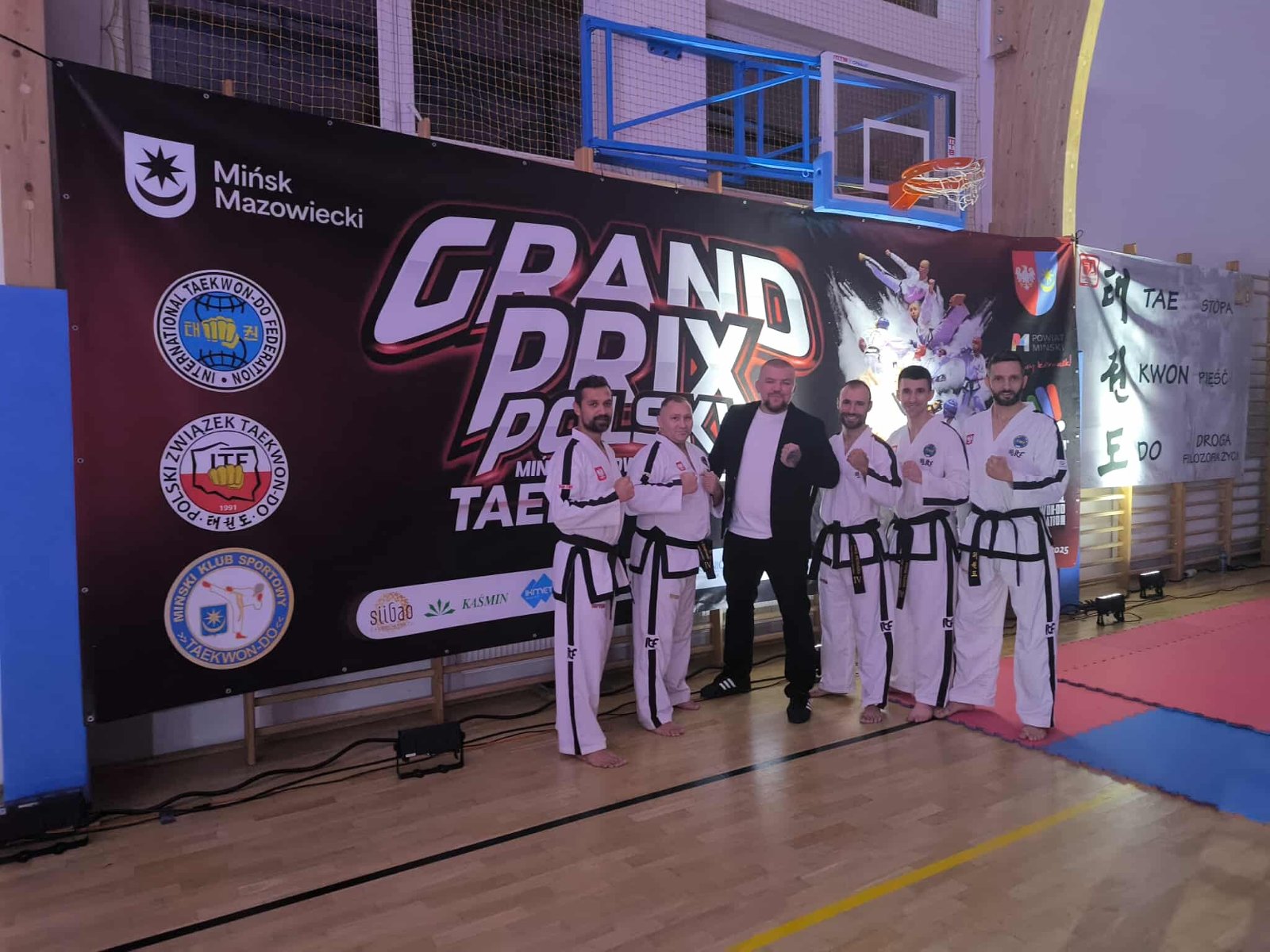 Zawodnicy PSKT na Grand Prix Polski w Taekwon-do - 6 osób na tle ścianki zawodów, 5 zawodników oraz prowadzący imprezę