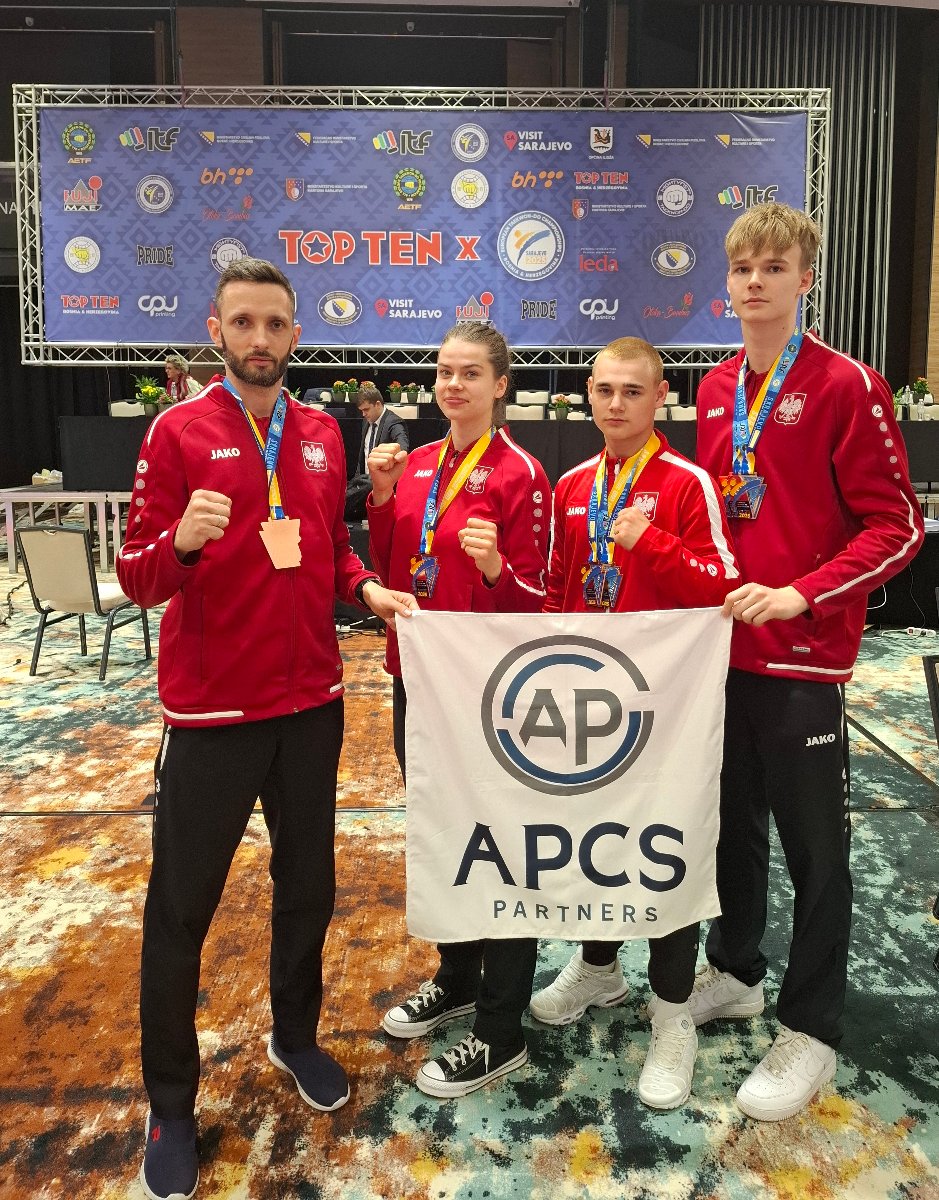 Zawodnicy PSKT na ME w Takewon-do w Sarajewie - 3 zawodników i 1 zawodniczka stoją w czerwonych bluzach reprezentacji Polski i na szyjach mają wywalczone medale. W rękach trzymają baner sponsora, a w tle widać scenę