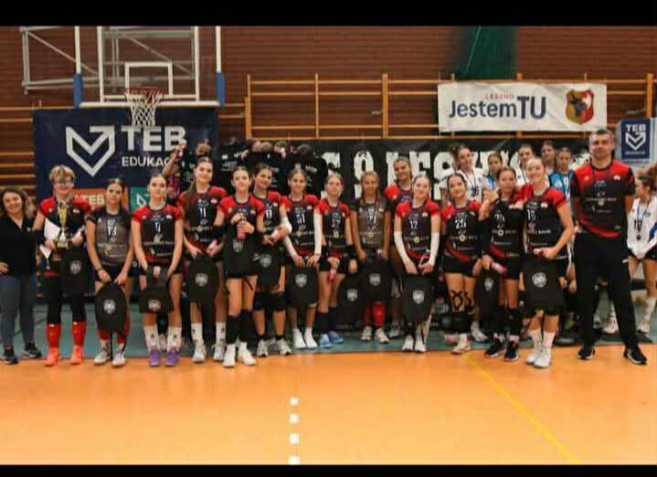 Zawodniczki SKF PBS SP 69 Poznań ze zwycięstwem w turnieju w Lesznie - zawodniczki wraz ze sztabem szkoleniowym stoją w strojach sportowych i trzymają w rękach nagrody na tle sali sportowej