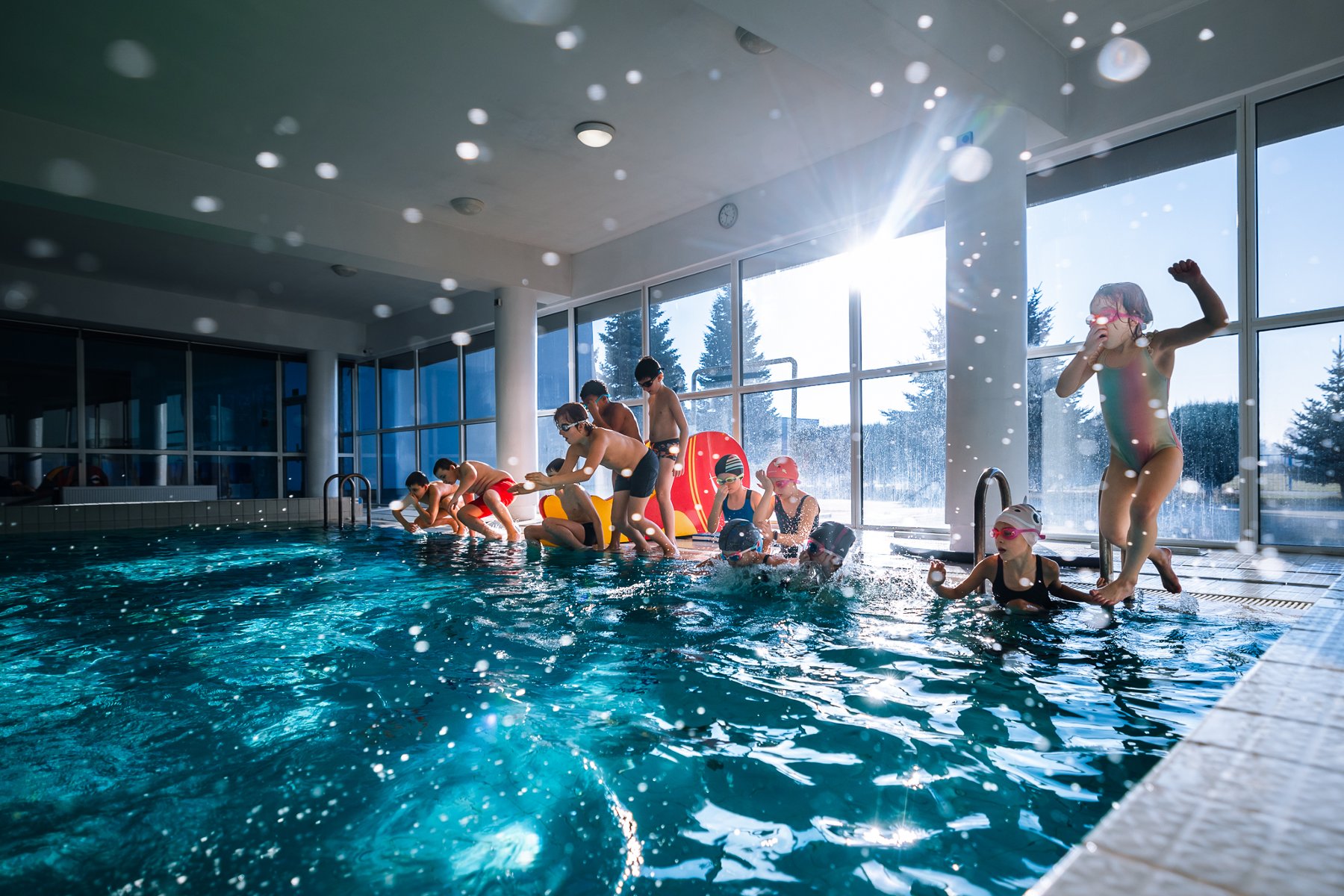 Zdjęcie przedstawia dzieci pływające na deskach w basenie.