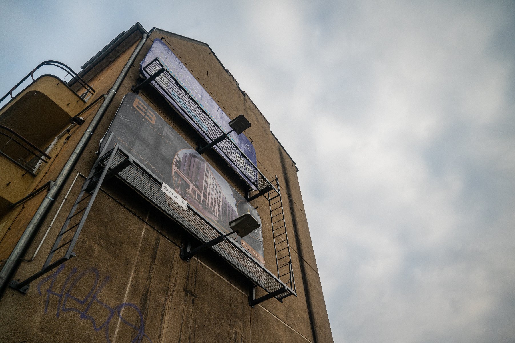 Zdjęcie przedstawia elewację kamienicy z zamontowanymi na niej dużymi nośnikami reklamowymi (billboardami).