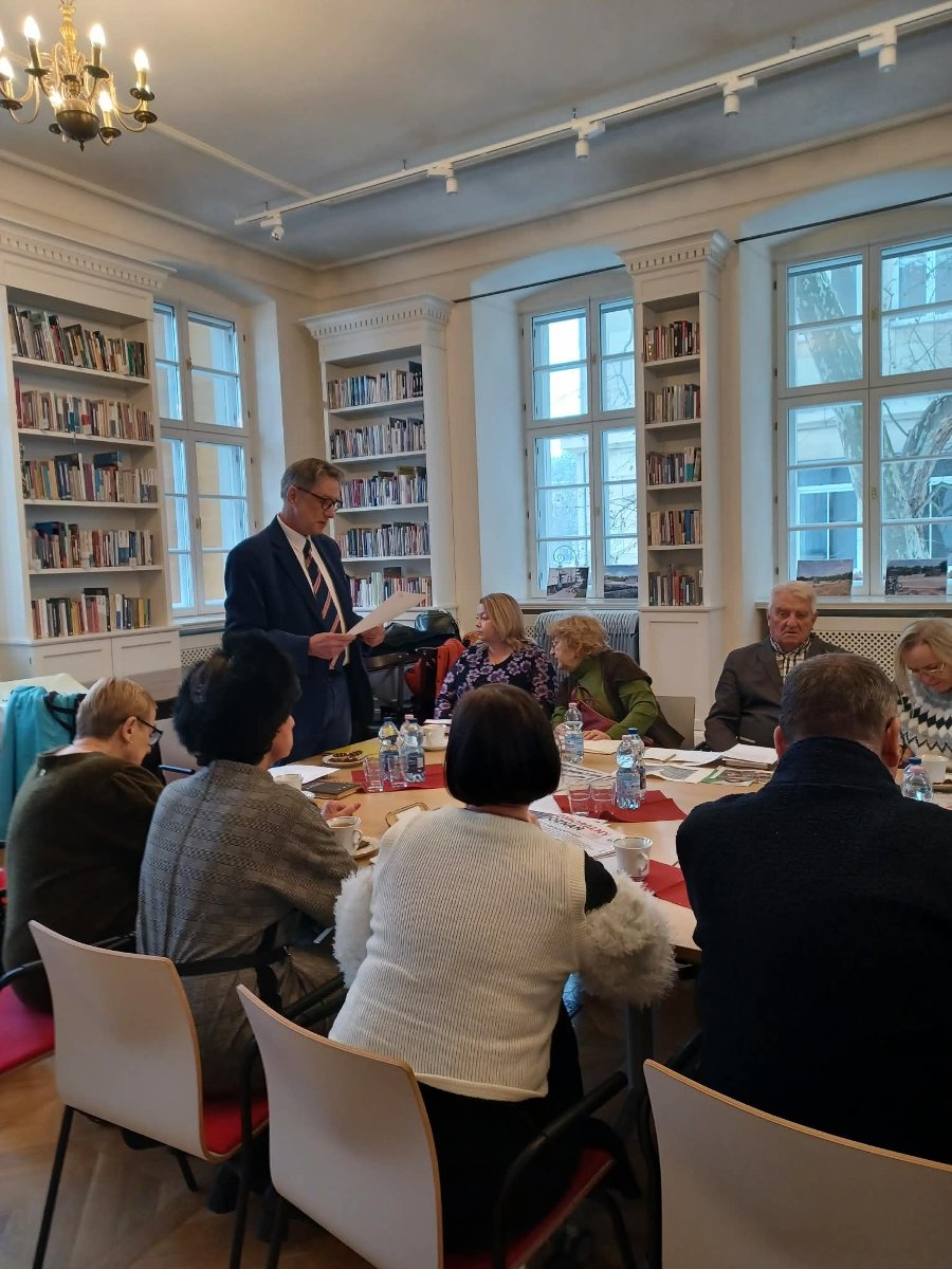 Zdjęcie przedstawia grupę seniorek i seniorów, którzy siedzą przy stole.