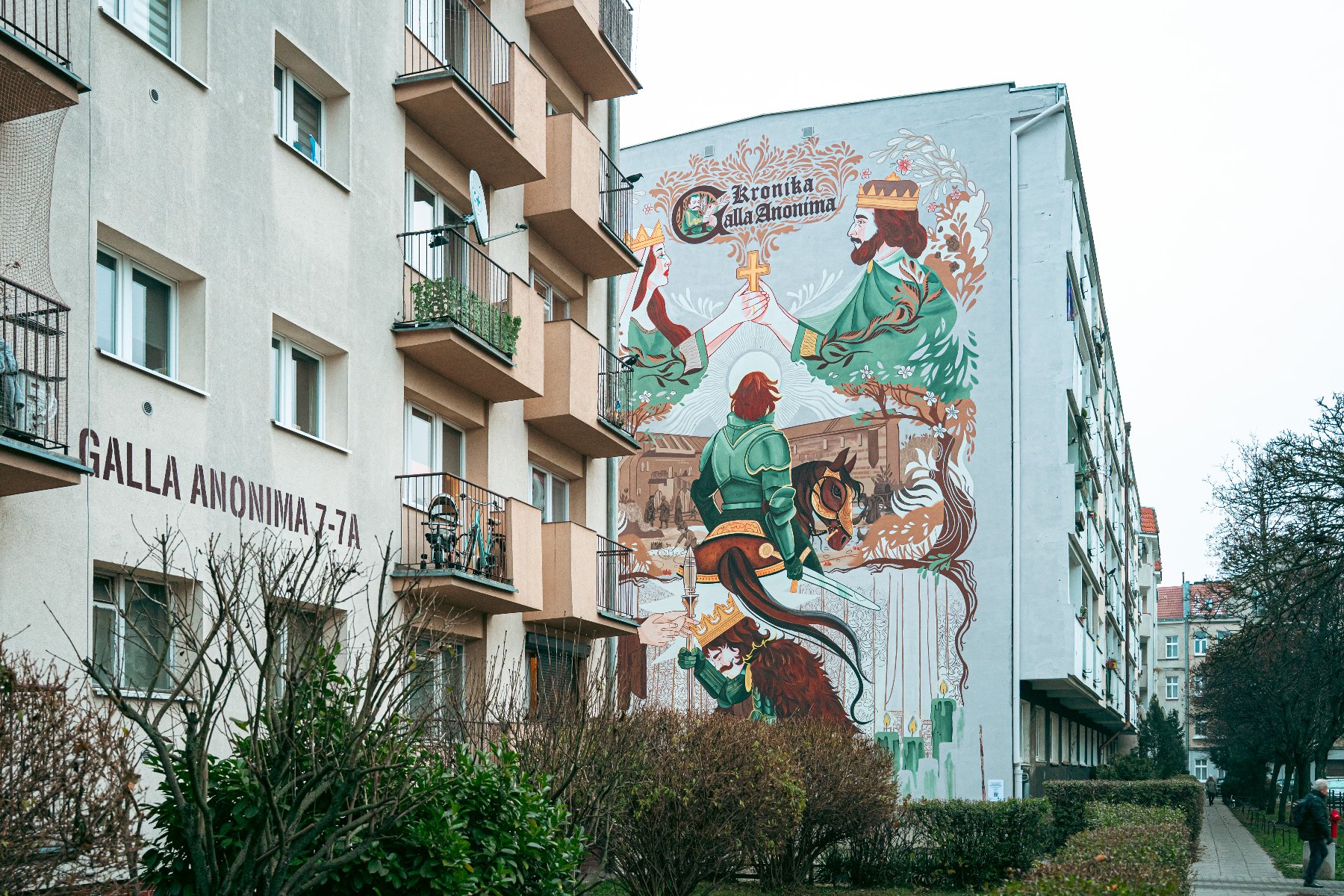 Zdjęcie przedstawia mural na budynku. Na muralu widać między innymi mężczyznę i kobietę w koronie czy mężczyznę na koniu.