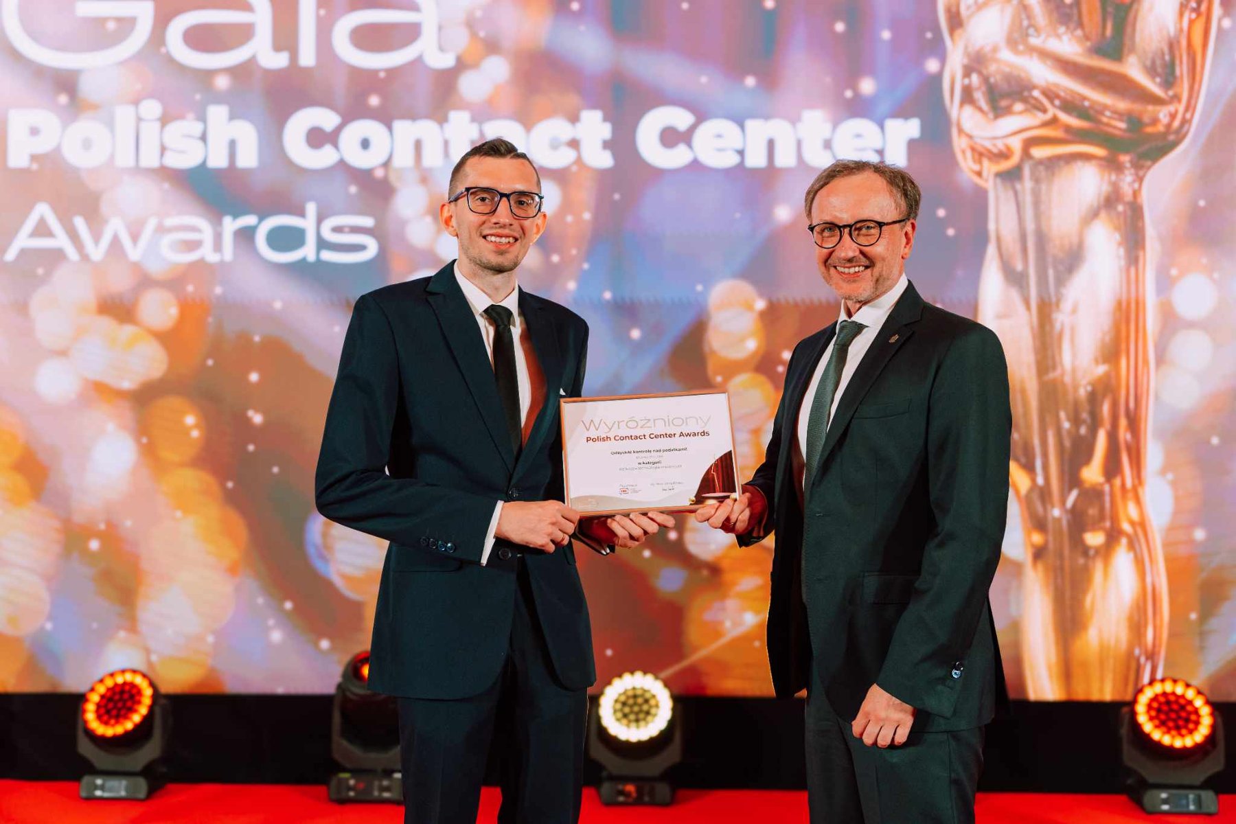 Wyróżnienie dla Biura Poznań Kontakt w konkursie PCCA 2025 Zdjęcie przedstawia pracownika biura Poznań Kontakt na tle loga PCCA