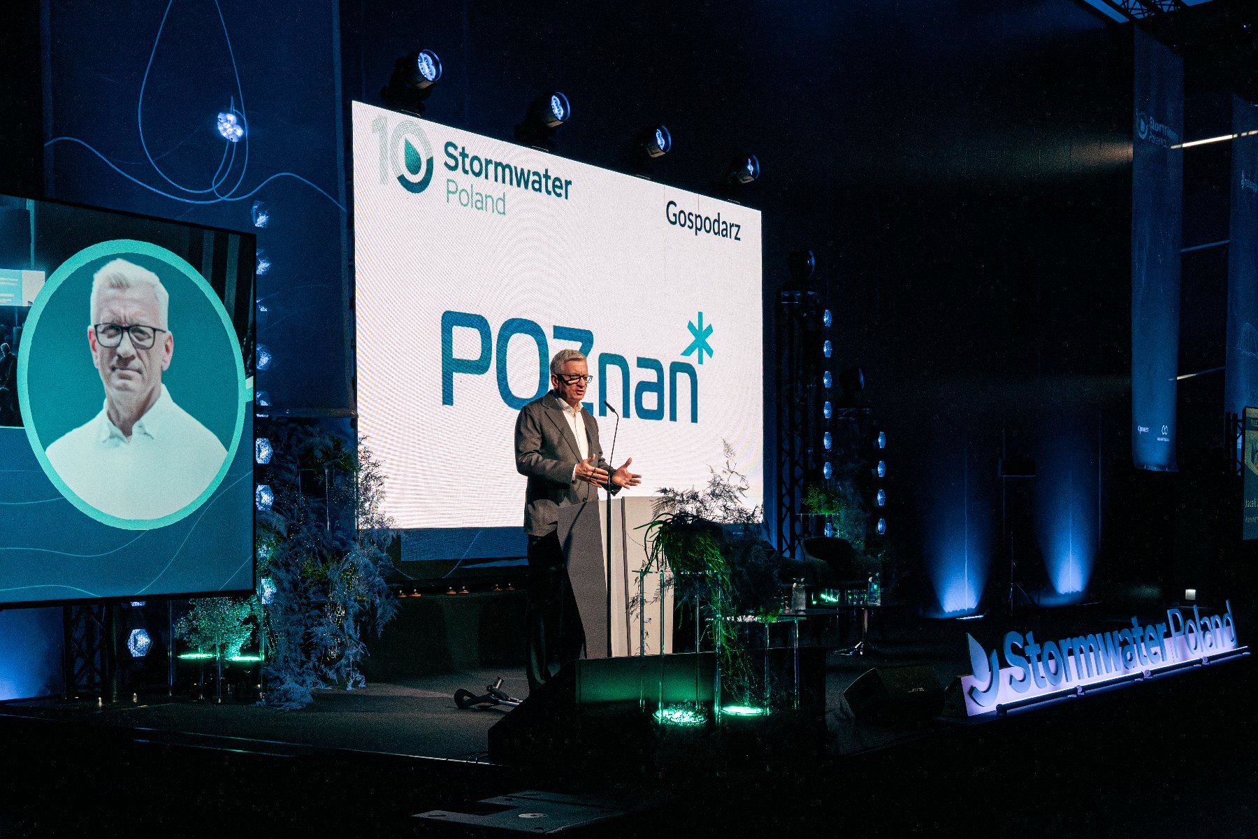 Zdjęcie przedstawia prezydenta Poznania na scenie przy mównicy. Na widowni na krzesłach siedzą ludzie.