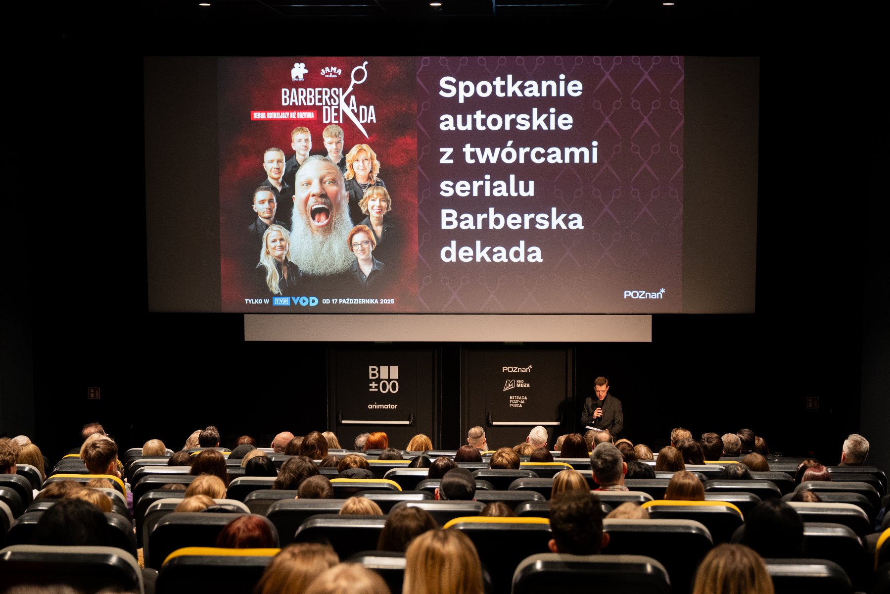 Zdjęcie przedstawia salę kinową. Na krzesłach siedzą młodzi ludzi, a na ekranie jest informacja o serialu i spotkaniu autorskim.