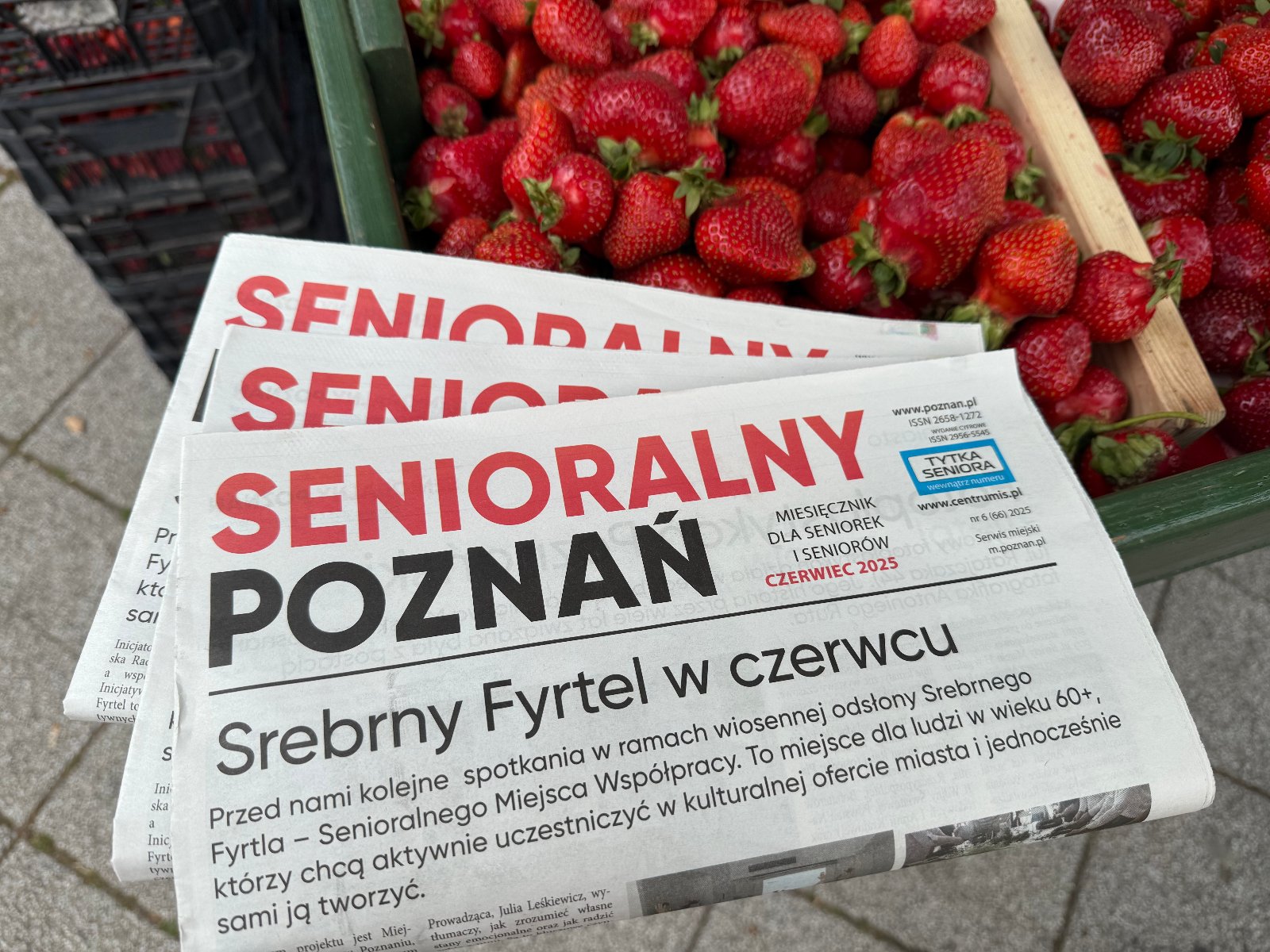 Senioralny Poznań - czerwiec 2025, fot. APS Zdjęcie przedstawia stragan z truskawkami na którym leży miesięcznik senioralny poznań na czerwiec 2025r.