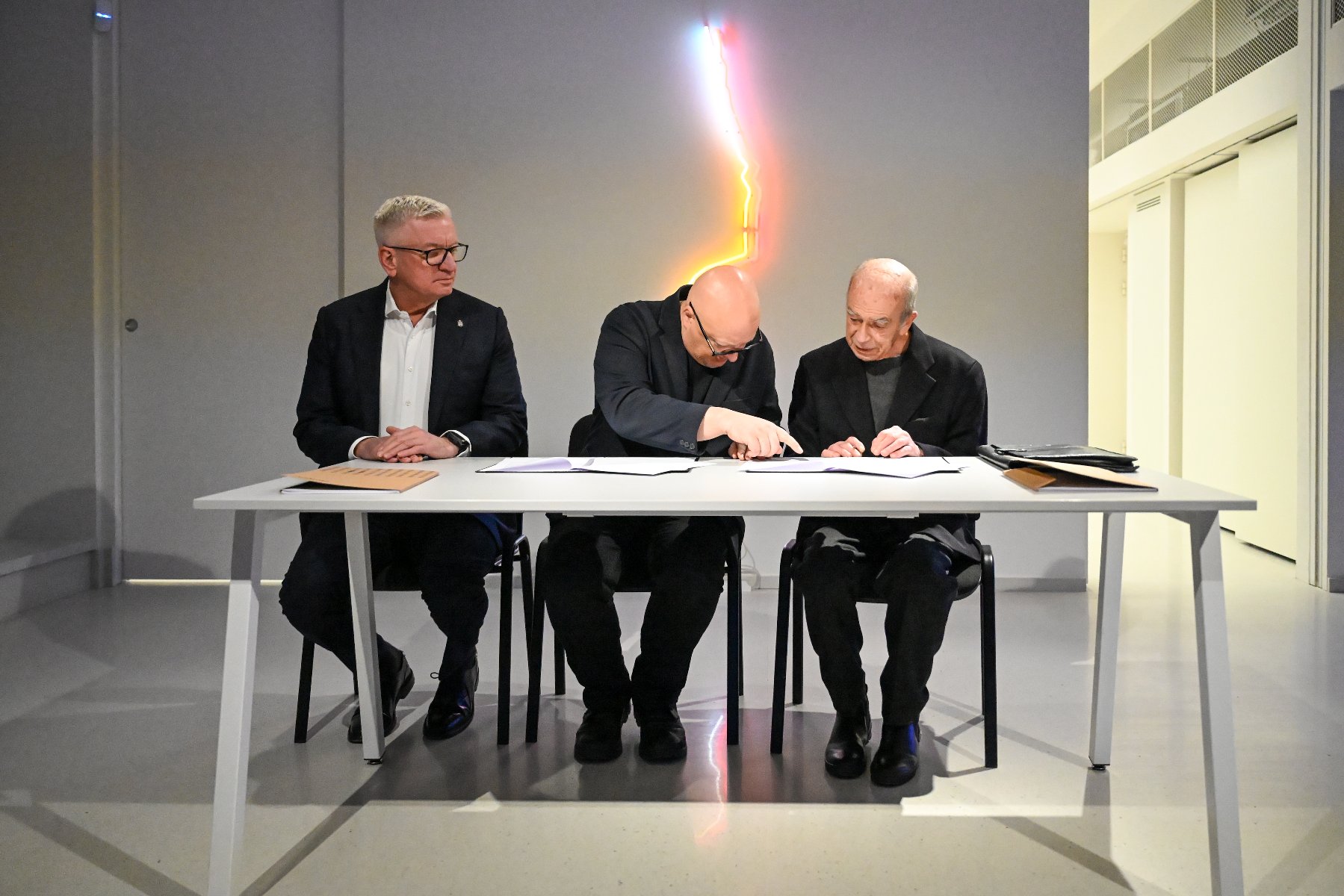 Zdjęcie przedstawia trzech mężczyzn. Dwóch podaje sobie ręke.