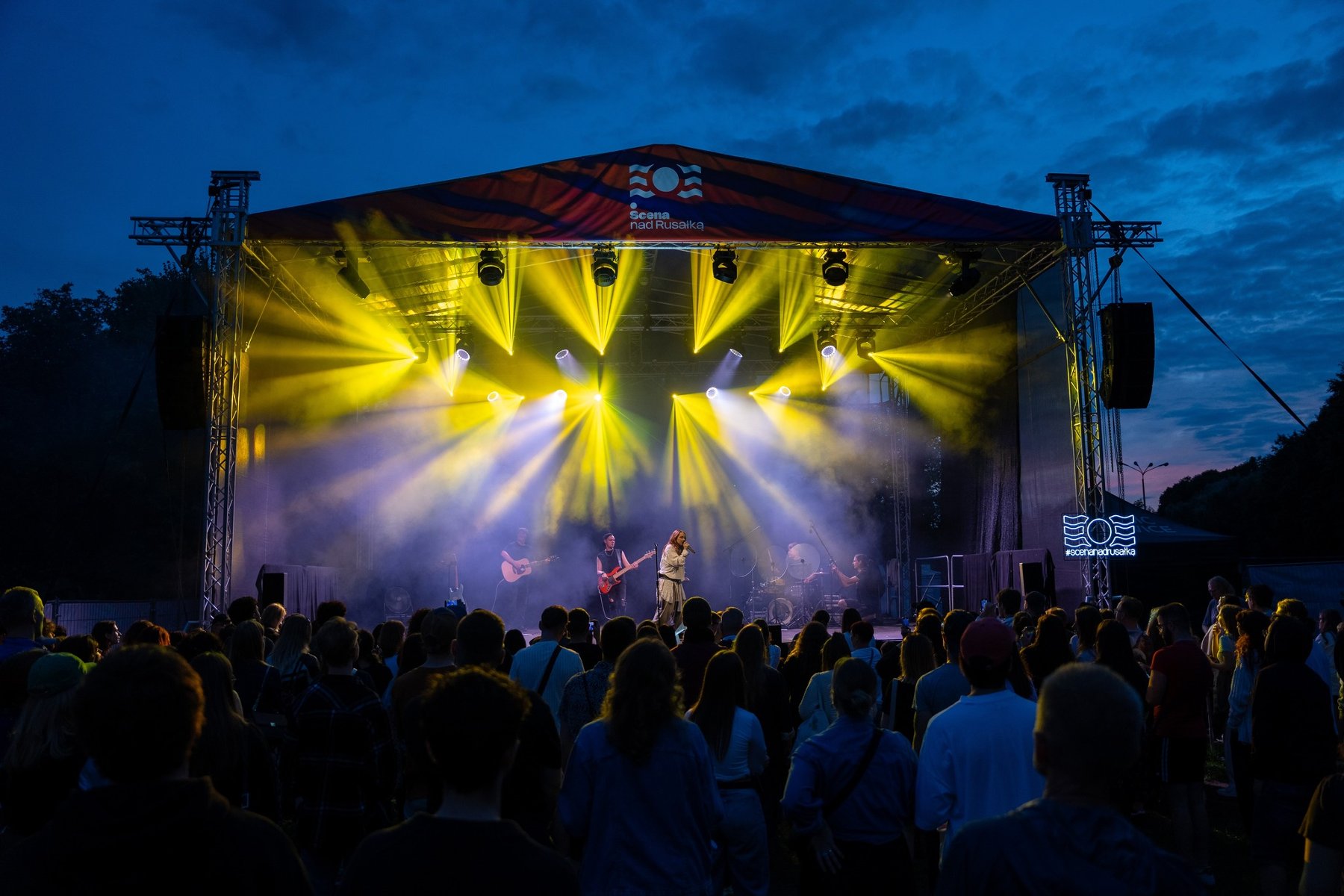 Zdjęcie rozświetlonej sceny podczas koncertu i publiczność stojąca przed nią