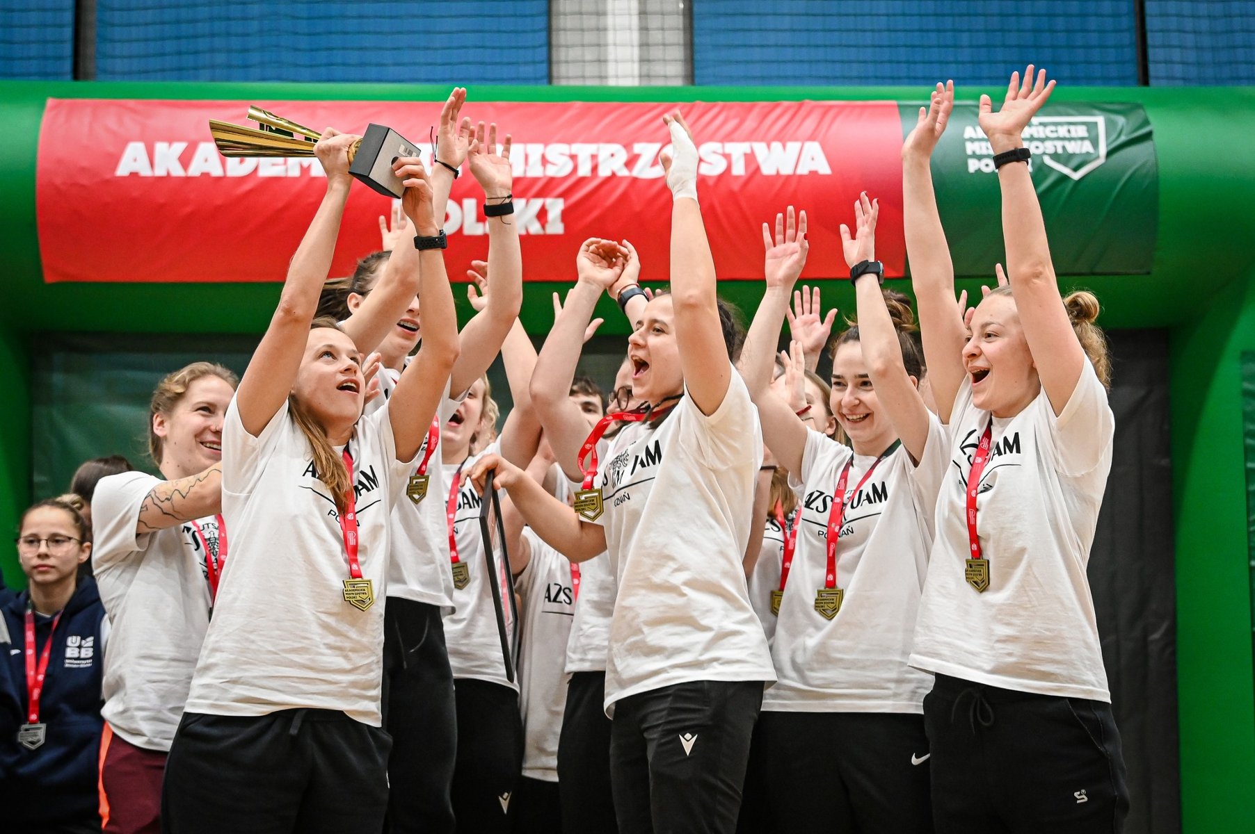 Akademickie Mistrzostwa Polski w futsalu, fot. AZS - zawodniczki AZS UAM Poznań cieszą sięw białych koszulkach, z medalami na szyi oraz pucharem w ręku jednej zawodniczek