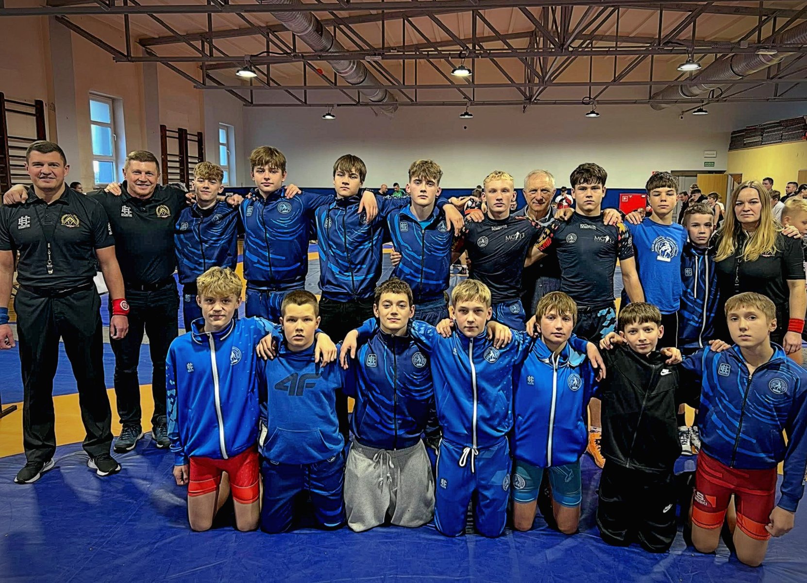 Drużyna Sobieskiego Poznań na Międzywojewódzkich Mistrzostwach Młodzików w zapasach, fot. Maciej Kula Drużyna Sobieskiego Poznań na Międzywojewódzkich Mistrzostwach Młodzików w zapasach, fot. Maciej Kula - z przodu zawodnicy kleczą na materacu w strojach klubowych. Za nimi stoją pozostali zawodnicy i trenerzy w strojach klubowych