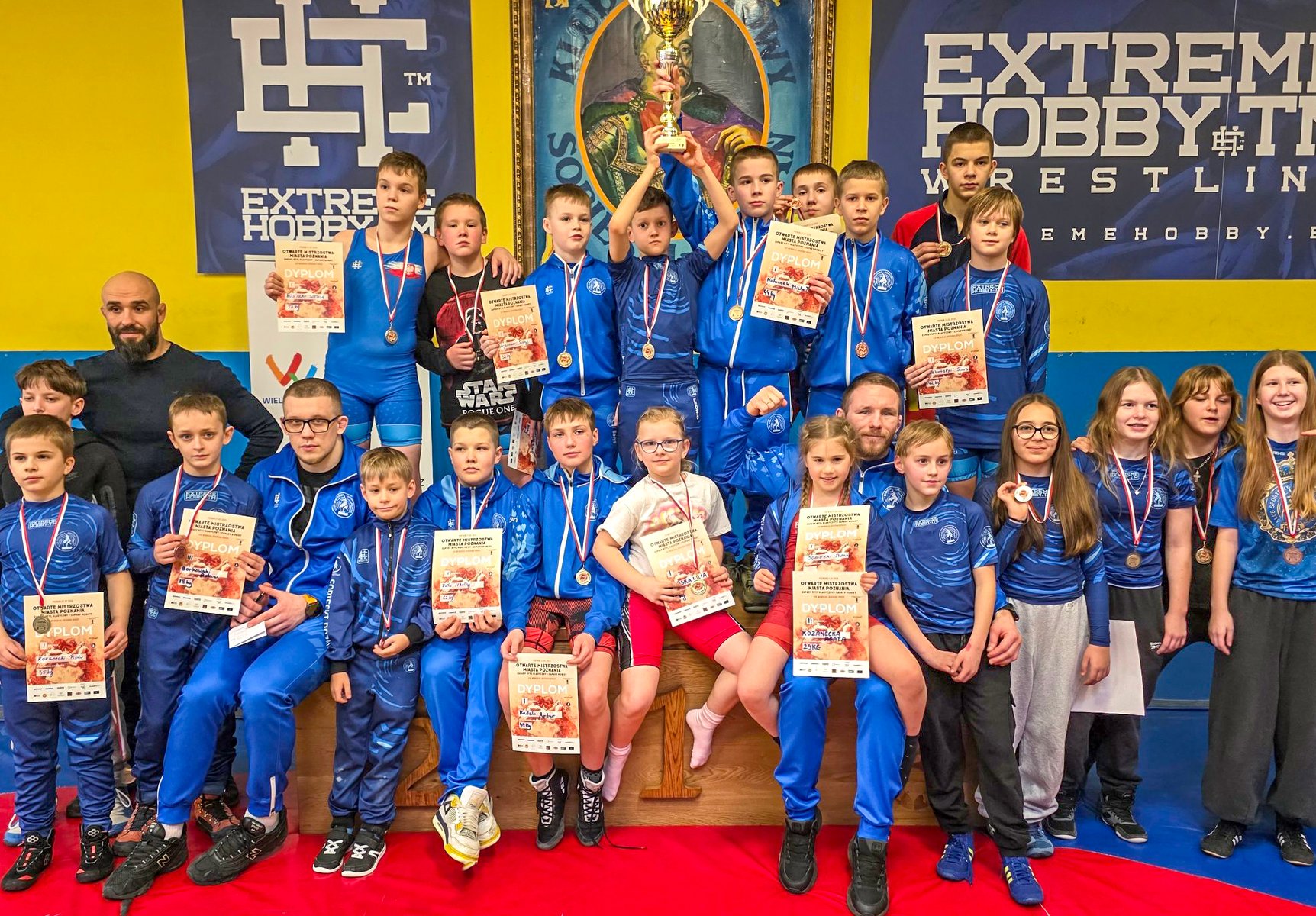 Memoriał Bogdana Brody w zapasach, fot. Maciej Kula - kilkanaścioro zawodników w strojach klubowych Sobieskiego siedzi i stoi z trenerami. Większość z nich ma medale oraz część z nich ma dyplomy