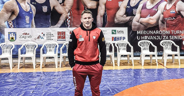 Tadeusz Michalik stojący na tle plakatu z chorwackimi zapaśnikami na Międzynarodowym Turnieju Zapaśniczym Zagreb Open 2021, fot. KS Sobieski Poznań