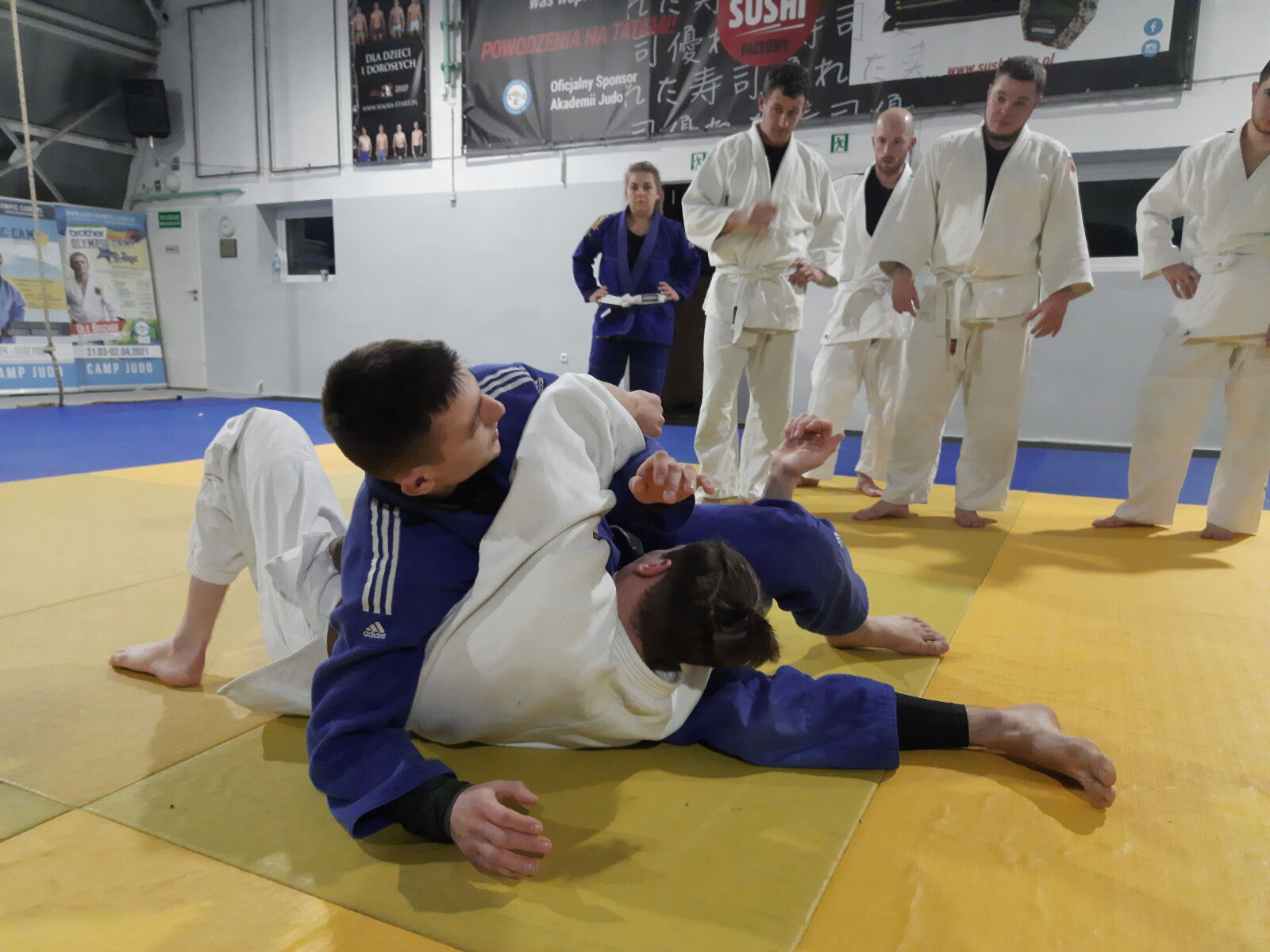 zawodnicy w białym i niebieskim judogo podczas pokazu walki na macie - grafika artykułu