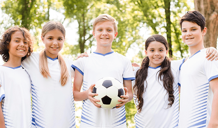 piątka dzieci w białych strojach sportowych, chłopiec na środku trzyma w rękach piłkę nożną - grafika artykułu