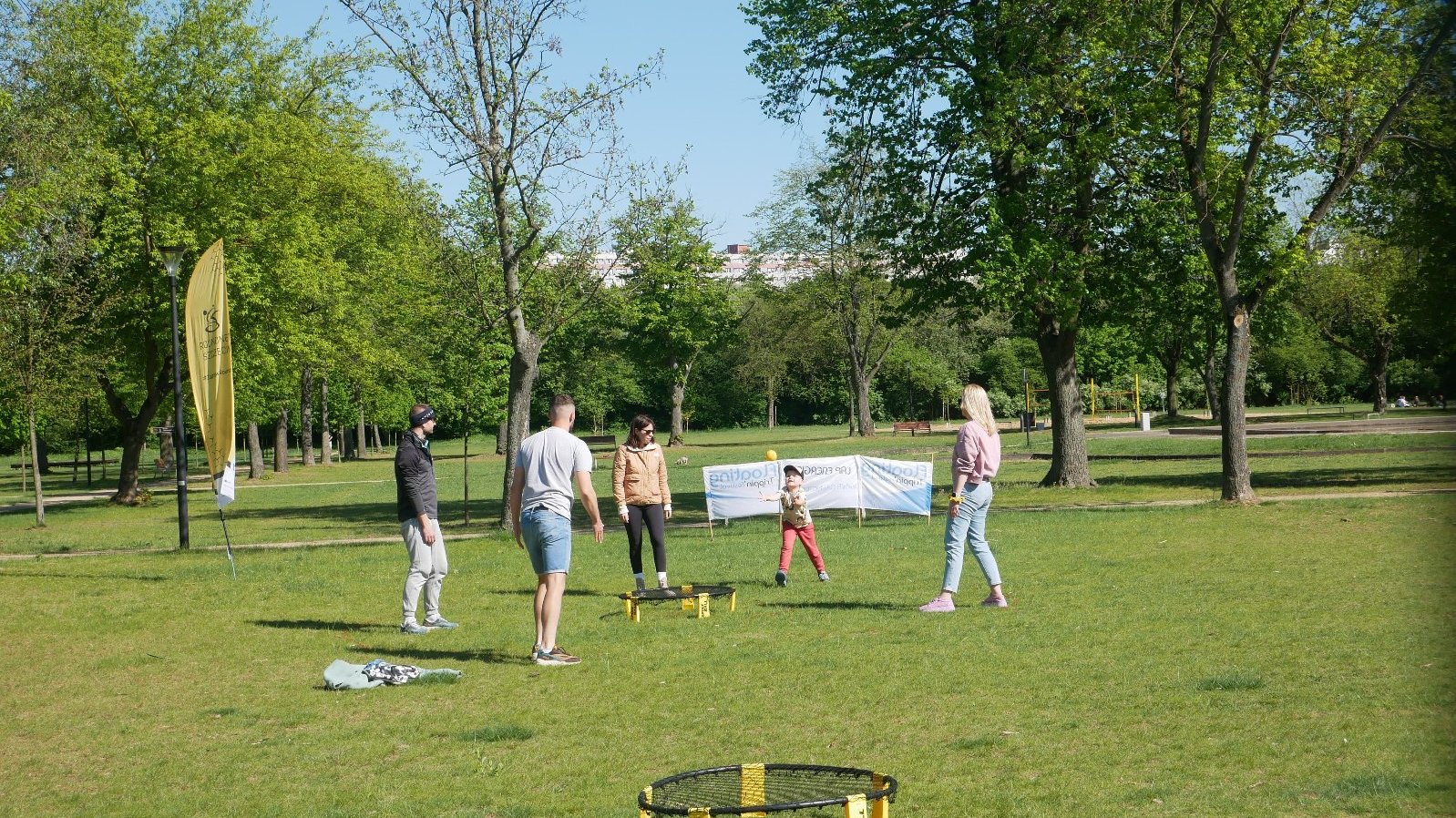 Strefa Sportu Poznań Roundnet Open 2025 - z przodu widać jedną trampolinę, a w oddali drugą wokół której 2 mężczyzn, 2 kobiety i 1 dziecko bawi się z piłką