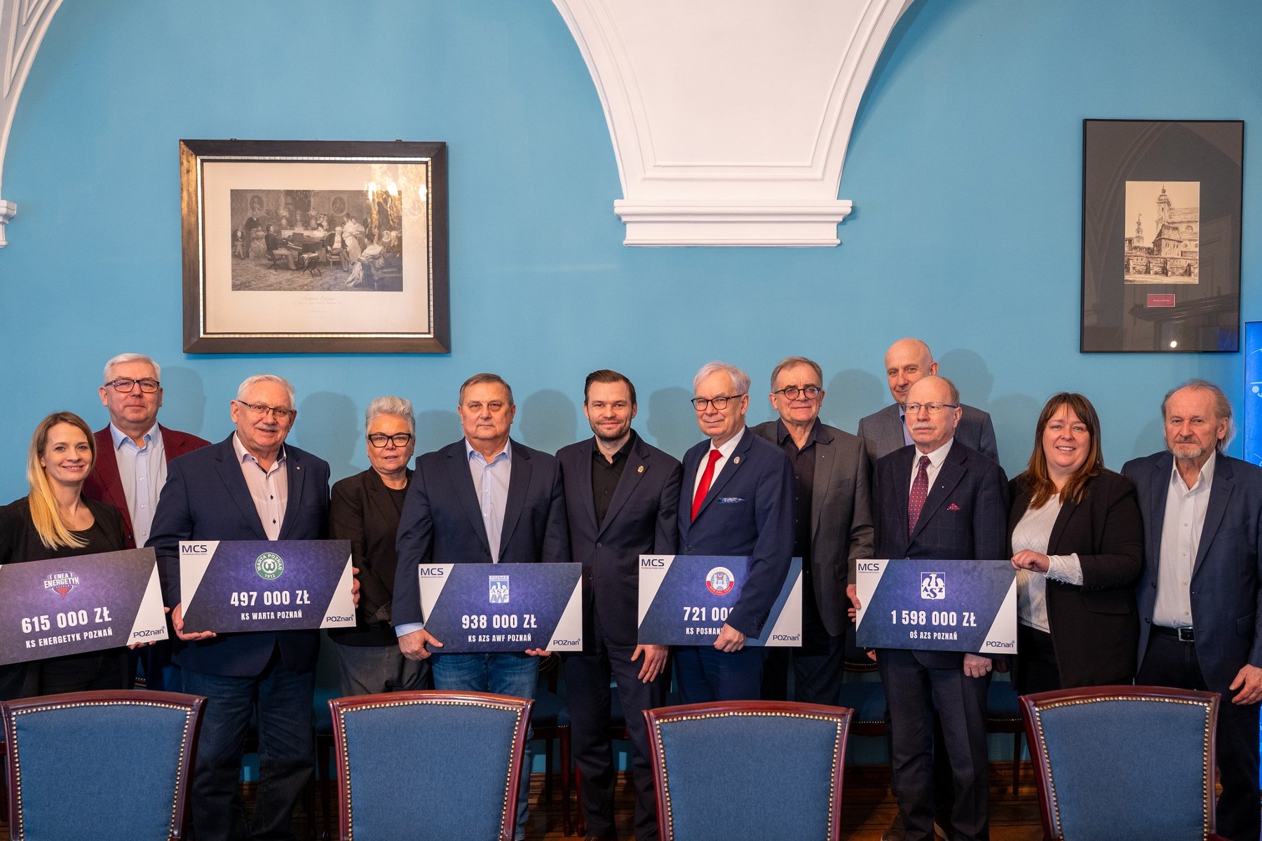 Podpisanie umów MCS z czołowymi poznańskimi klubami sportowymi, fot. Biuro Prasowe UMP - kilkanaście osób elegancko ubranych pozuje do zdjęcia, z tego kilka osób z nich trzyma czeki