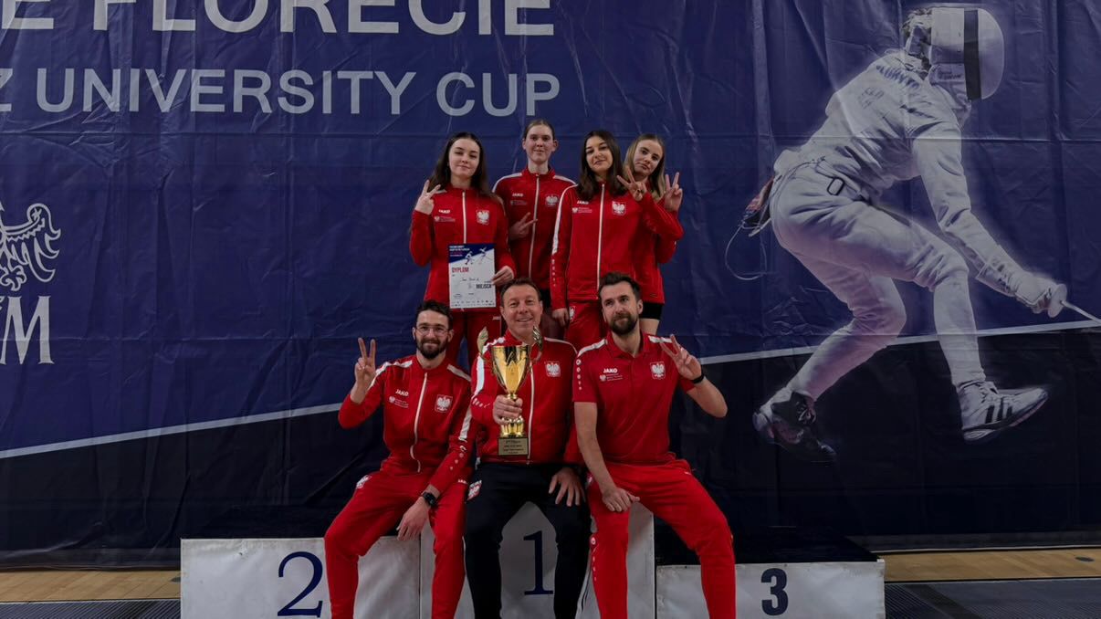 Polskie zawodniczki na podium Pucharu Europy Kadetek we florecie, fot. Facebook Polski Związek Szermierczy - na podium stoją 4 zadowolone zawodniczki, z których jedna trzyma dyplom. Poniżej siedzi 3 mężczyzn, prawdpopodobnie członków sztabu szkoleniowego, którzy również są zadowoleni, a jeden z nich trzyma puchar. Wszyscy są ubrani w czerwone stroje reprezentacji Polski