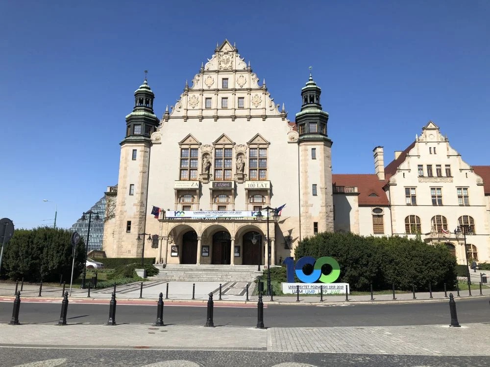 Front okazałego, jasnego budynku w stylu historycznym z dwiema wieżami i dużym wejściem na kolumnach