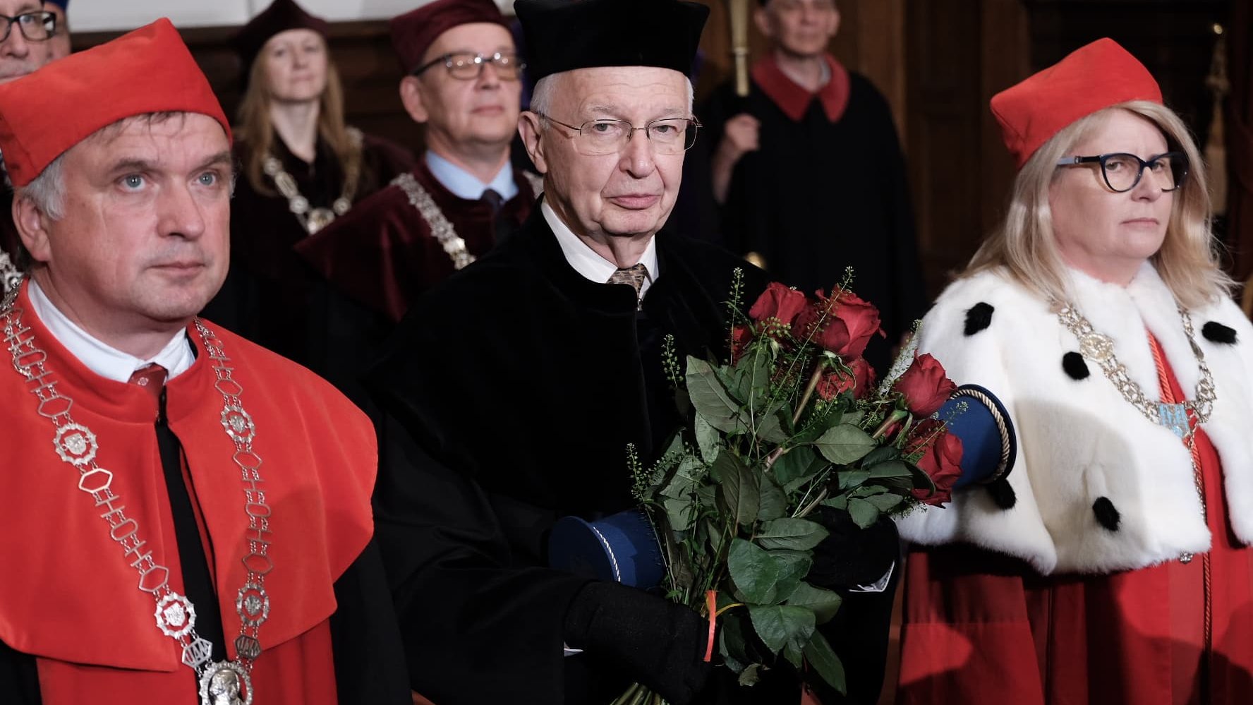 zdjęcie z uroczystego nadania tytułu doktora honoris causa UAM Prof. Jean-Marie Lehnowi, przedstawia laureata w czarnej todze, z bukietem kwiatów - grafika artykułu