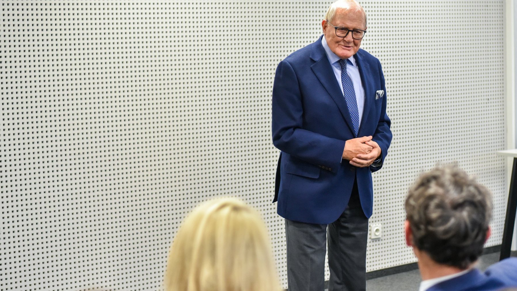 Zdjęcie przedstawia mężczyznę w garniturze przemawiającego w sali konferencyjnej