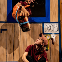 Sena z przedstawienia: przy drewnianej ścianie siedzi kobieta, która patrzy na konia (pacynkę) wystawiajacego łeb przez otwór w ścianie.