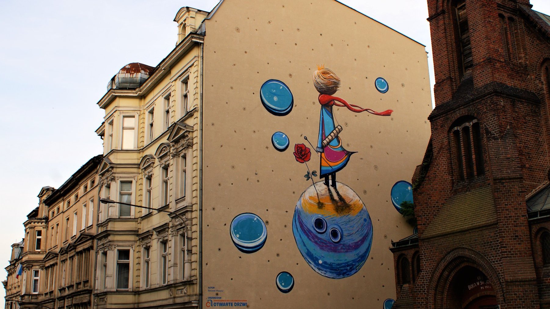Kamienica i fragment zabytkowego kościoła. Na ścianie kamienicy mural Małego Księcia.