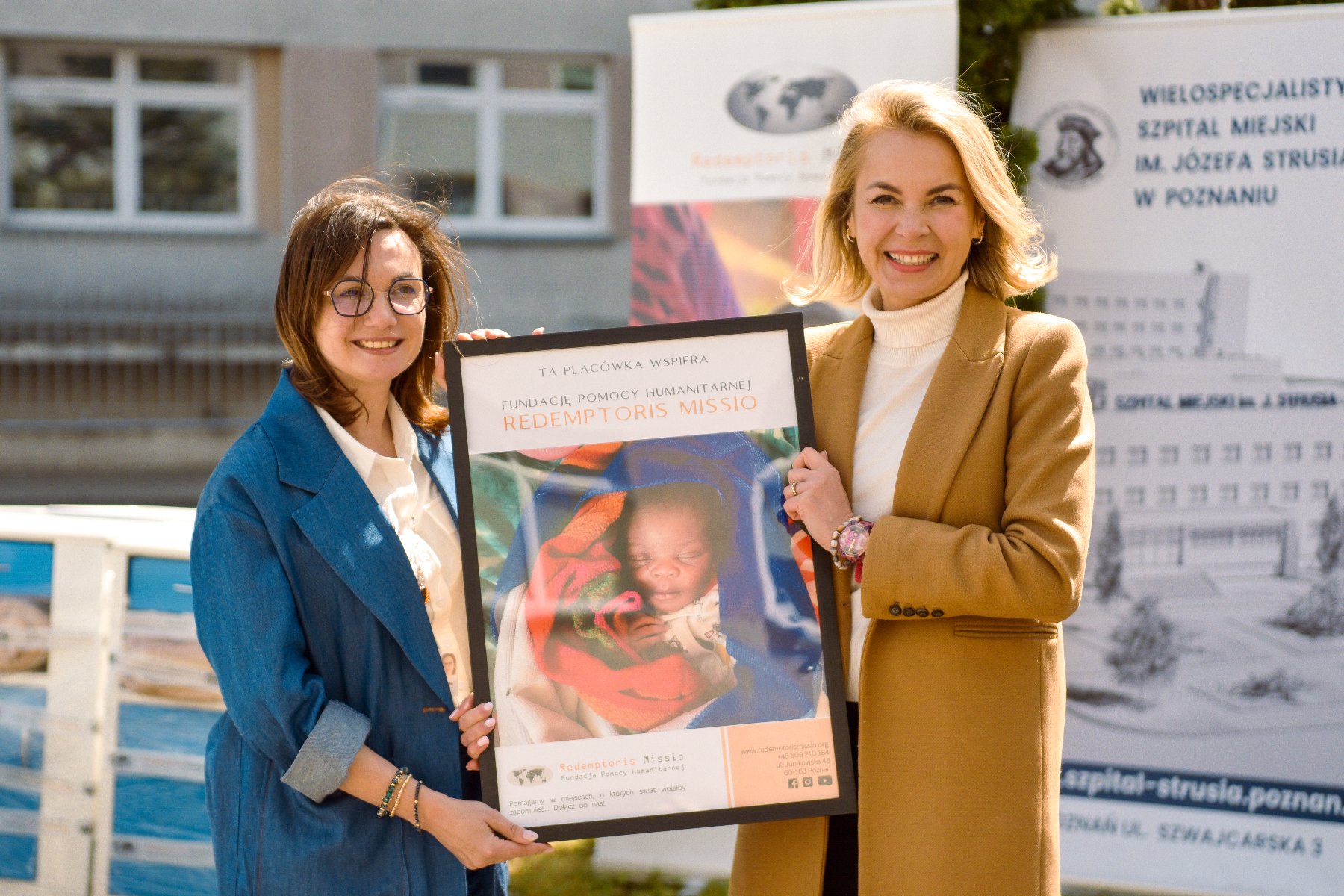 Sprzęt z poznańskiego szpitala trafi do Republiki Środkowoafrykańskiej Na zdjęciu dwie kobiety trzymające plakat, na nim małe dziecko