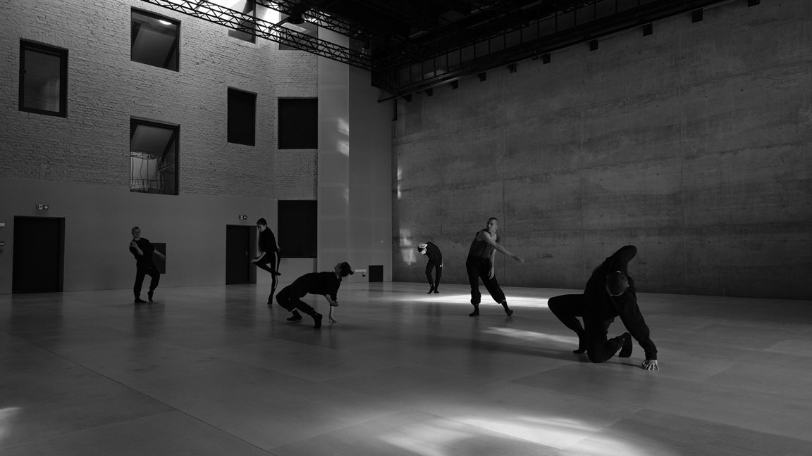 Black and white photo of dancers in various poses in empty, modern space. - grafika artykułu