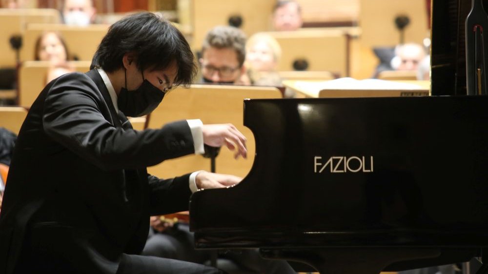 Picture from the concert: Bruce Liu playing the piano. Members of the orchestra in the background