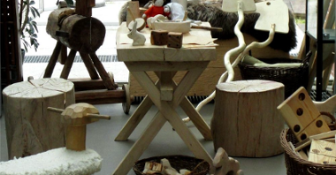 Wooden furniture (a table, two stools), wooden toys (horses, some small toys) and wicker baskets filled with various things. On the right a wicker basket with wooden big dominoes.