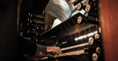 A part of pipe organ. The photo shows a musician's hands on a keyboard and pages with notes