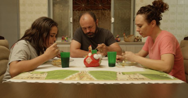 Photo from the movie: three people (a woman, a girl and a man) sitting at the table and eating. Each of them is looking at the plate.