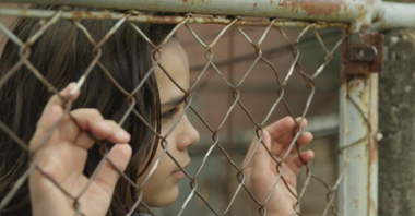Photo from the movie: a girl standing by the metal fence, holding it and looking somewhere