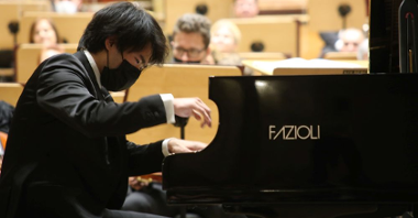 Picture from the concert: Bruce Liu playing the piano. Members of the orchestra in the background