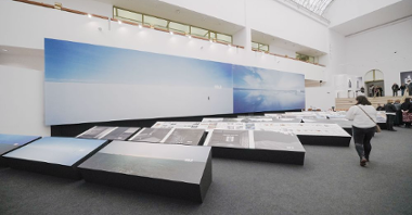 Photo of the exhibition hall with two big pictures hanging on the wall and other pictures displayed on low expositors.