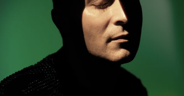 Photo of Michał Pepol, with his face illuminated; green background.