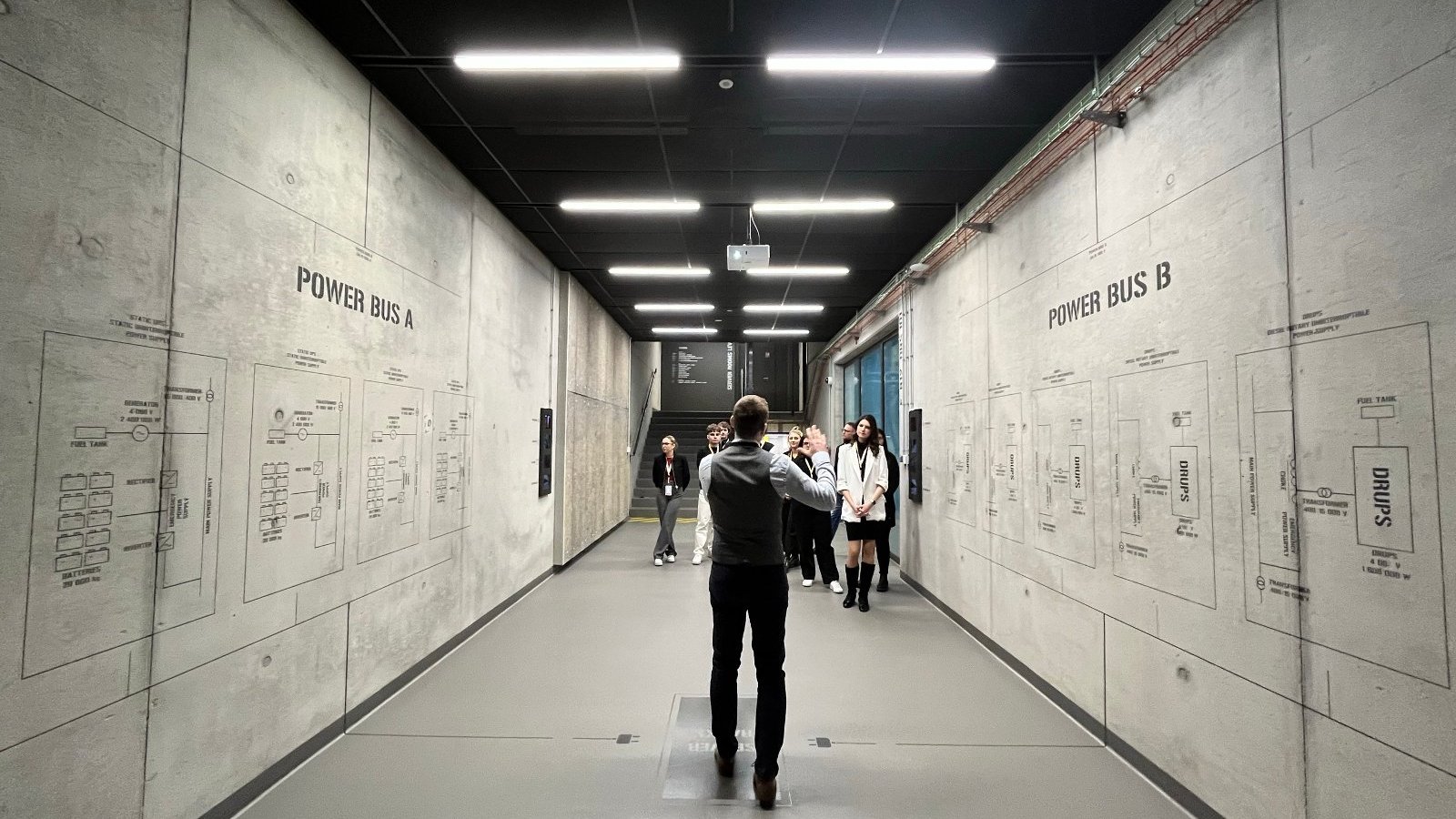 The picture shows several people listening to the speaker in a wide corridor