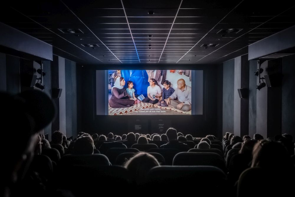 Audiences in the cinema watch a movie on a big screen. It is dark, the room is illuminated only by the light from the screen. - grafika artykułu