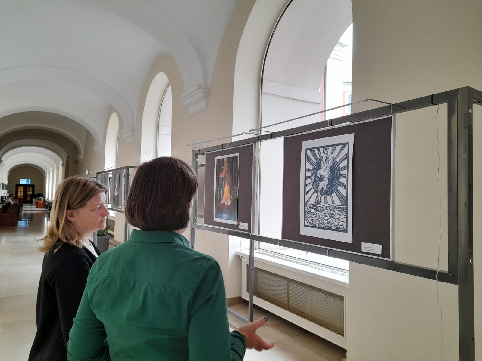 In the photo we see two women standing with their backs looking at the exhibition - grafika artykułu