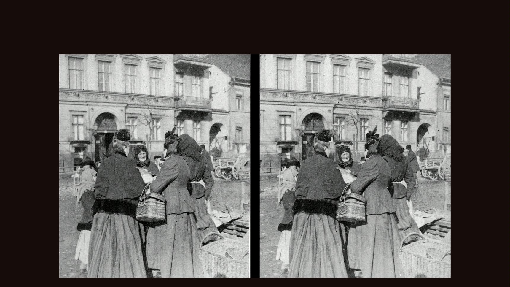 Black and white stereophotograph of a few peddler women standing together. One of them is holding a wicker basket. Two buildings as a background.