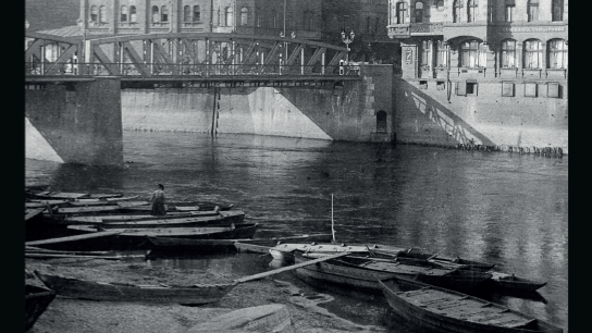 Black and white photo of the river, a few boats, the bridge and buildings along the river. Below the photo, information about the exhibition.