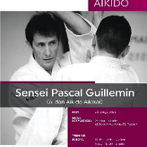 Czarno-białe zdjęcie mężczyzny podpisanego jako "Sensei Pascal Guillemin (6. dan Aikido Aikikai)", rozmawiającego z inną osobą podczas treningu.
