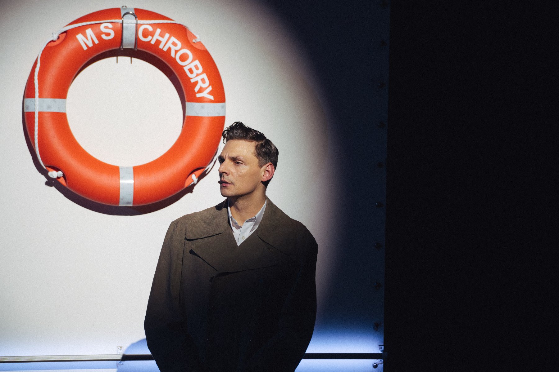 Rejs w Teatrze Nowym, fot. materiały prasowe Aktor na scenie, za nim koło ratunkowe statku M/S Chrobry
