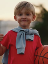 Chłopiec trzyma piłkę, drugą ręką pokazującgest kciuka do góry.