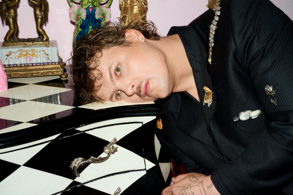 fot. materiały prasowe Artysta trzyma przed sobą złotą, bogato zdobioną, okrągłą ramę, przez którą widać jego twarz.