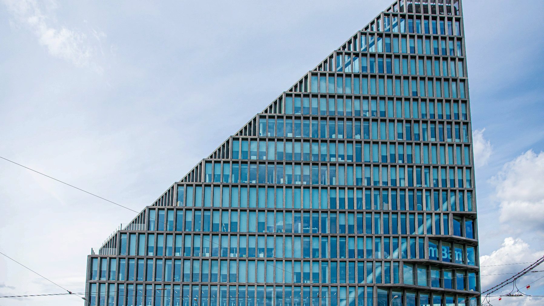Galeria zdjęć przedstawia wieżowiec biurowy o szklanej elewacji opartej o szare betonowe słupy.