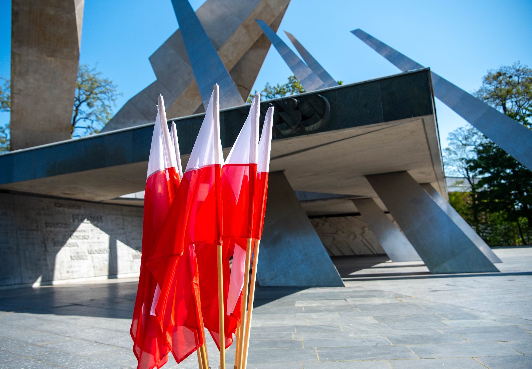 W stolicy Wielkopolski uroczystości odbyły się pod pomnikiem upamiętniającym żołnierzy Armii Poznań Ceremonia upamiętniająca. Na pierwszym planie żołnierz w mundurze składa duży zielony wieniec na stojaku. Obok niego stoi grupa osób ubranych formalnie, w tym wojskowi i cywile. W tle drzewa i słoneczna pogoda.