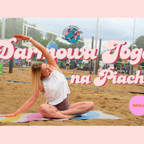 Kobieta siedzi po turecku na ręczniku na piachu i rozciąga lewą rękę nad głową w prawą stronę.