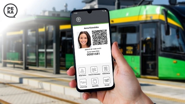 Fot. ZTM Poznań dłoń trzyna telefon komórkowy, na ekranie wyświetona twarz kobiety i QR kod, w tle za telefonem wiata przystankowa i tramwaj